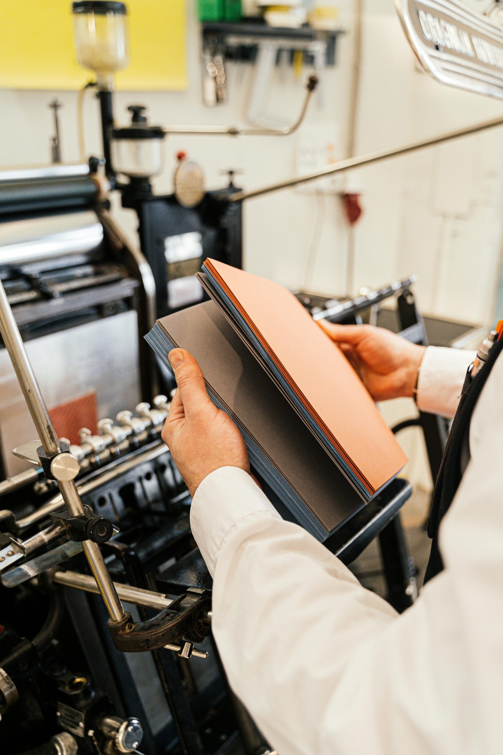 Person holding papers near a printing press in a workshop setting.